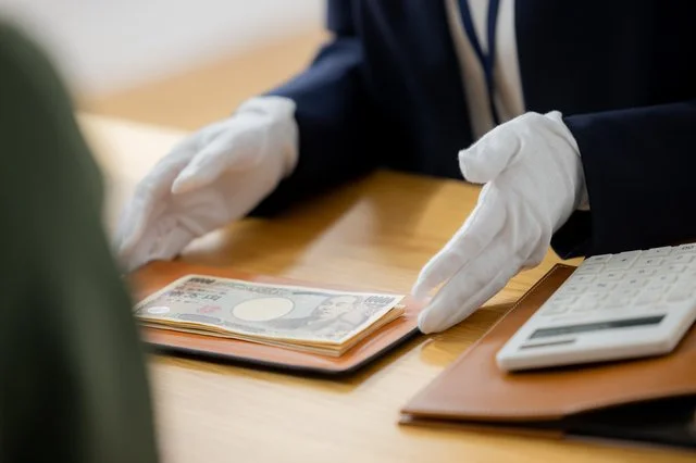 白手袋をつけたスタッフが、一万円札の束と電卓を前にお客様へ対応している様子